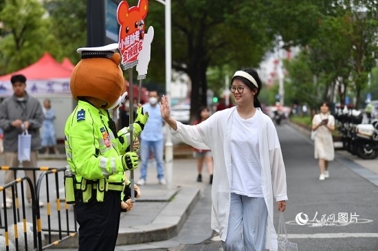 6月7日上午9時(shí)，隨著鈴聲的響起，2023年江西高考正式開考，江西省的53.57萬考生以縣（區(qū)）為單位隨機(jī)安排在全省256個(gè)考點(diǎn)、18968個(gè)考場參加高考。圖為“小熊交警”和考生擊掌鼓勵(lì)。 人民網(wǎng)記者 時(shí)雨攝