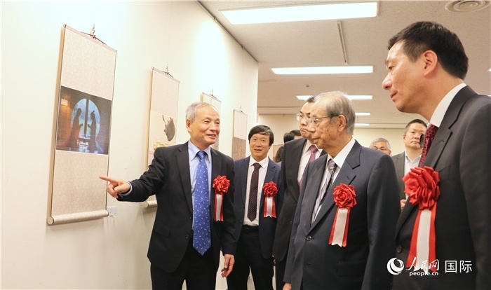 “湖州印象”攝影展主創(chuàng)、世界華人攝影協(xié)會副會長馮學(xué)敏向吳江浩大使、福田康夫前首相等嘉賓介紹展出作品。（人民網(wǎng) 許可攝）