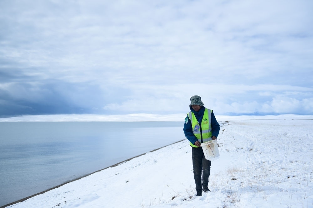 2021年10月20日，在青海省果洛藏族自治州瑪多縣扎陵湖鄉(xiāng)勒那村，三江源國家公園黃河源園區(qū)生態(tài)管護(hù)員在扎陵湖邊撿拾垃圾。新華社記者 張龍 攝
