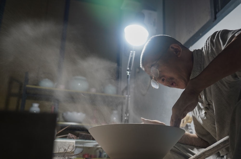 ↑ 在景德鎮(zhèn)，手工匠人吹去坯內的泥土（2021年7月14日攝）。