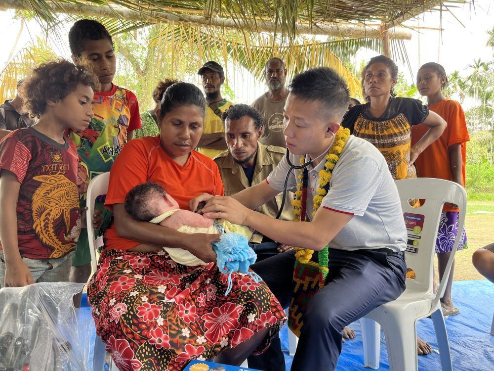 2023年8月5日，在巴布亞新幾內(nèi)亞中央省的一個村莊里，第12批援巴新中國醫(yī)療隊副隊長、新生兒科副主任醫(yī)師劉振球為嬰兒泰樂聽診檢查。泰樂出生時患有重癥，一度生命垂危，經(jīng)過劉振球與當(dāng)?shù)蒯t(yī)護人員的救治最終痊愈。從2002年起，中國連續(xù)向巴新派出12批醫(yī)療隊，為提高巴新醫(yī)療衛(wèi)生水平作出積極貢獻。