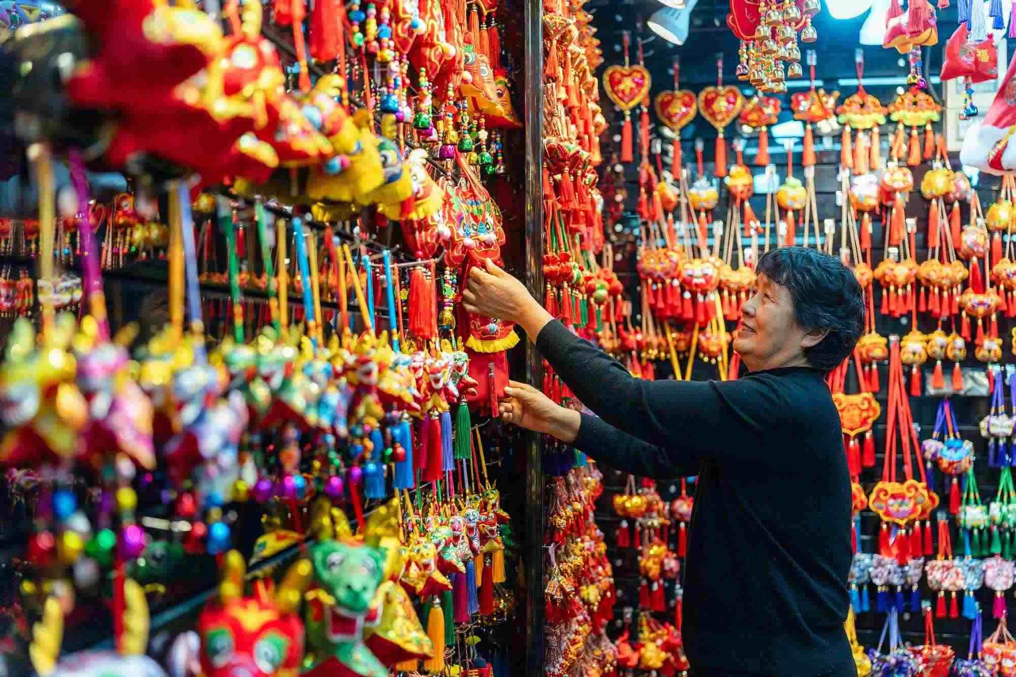 2023年12月11日，金華義烏國際商貿(mào)城，龍年喜慶用品掛滿攤位，顧客正在挑選中。