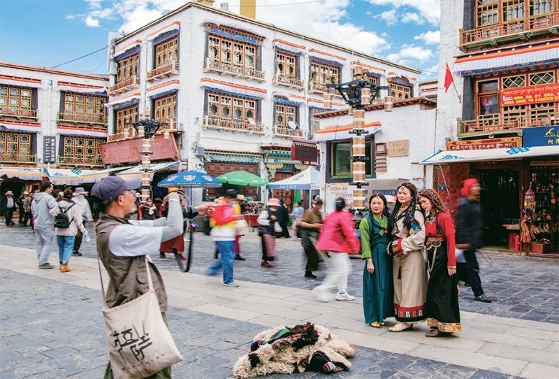 千年八廓街，見證民族團(tuán)結(jié)。2021年7月，習(xí)近平總書記來到位于西藏拉薩老城區(qū)的八廓街，感慨地說：“千年八廓街，是我們各民族建起來的八廓街。各民族文化在這里交流交往交融，我們中華民族的大家庭在這里其樂融融?！眻D為2023年6月13日，游客身著藏裝在八廓街拍照留念。 新華社記者 姜帆/攝