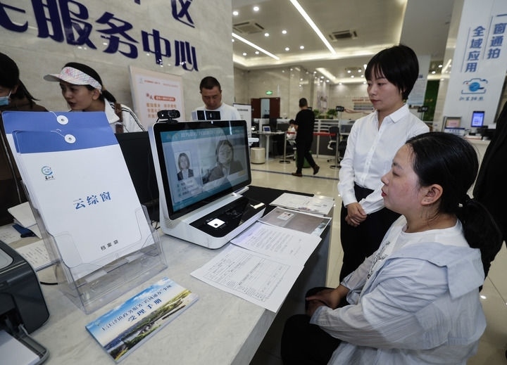 在浙江省嘉興市秀洲區(qū)王江涇鎮(zhèn)便民服務(wù)中心的“跨域通辦·云綜窗”窗口，辦理開業(yè)登記的個體工商戶（右一）通過該系統(tǒng)與江蘇省蘇州市吳江區(qū)盛澤鎮(zhèn)行政審批局工作人員視頻連線，進行身份讀取及材料線上審核（2024年5月9日攝）。新華社記者 徐昱 攝