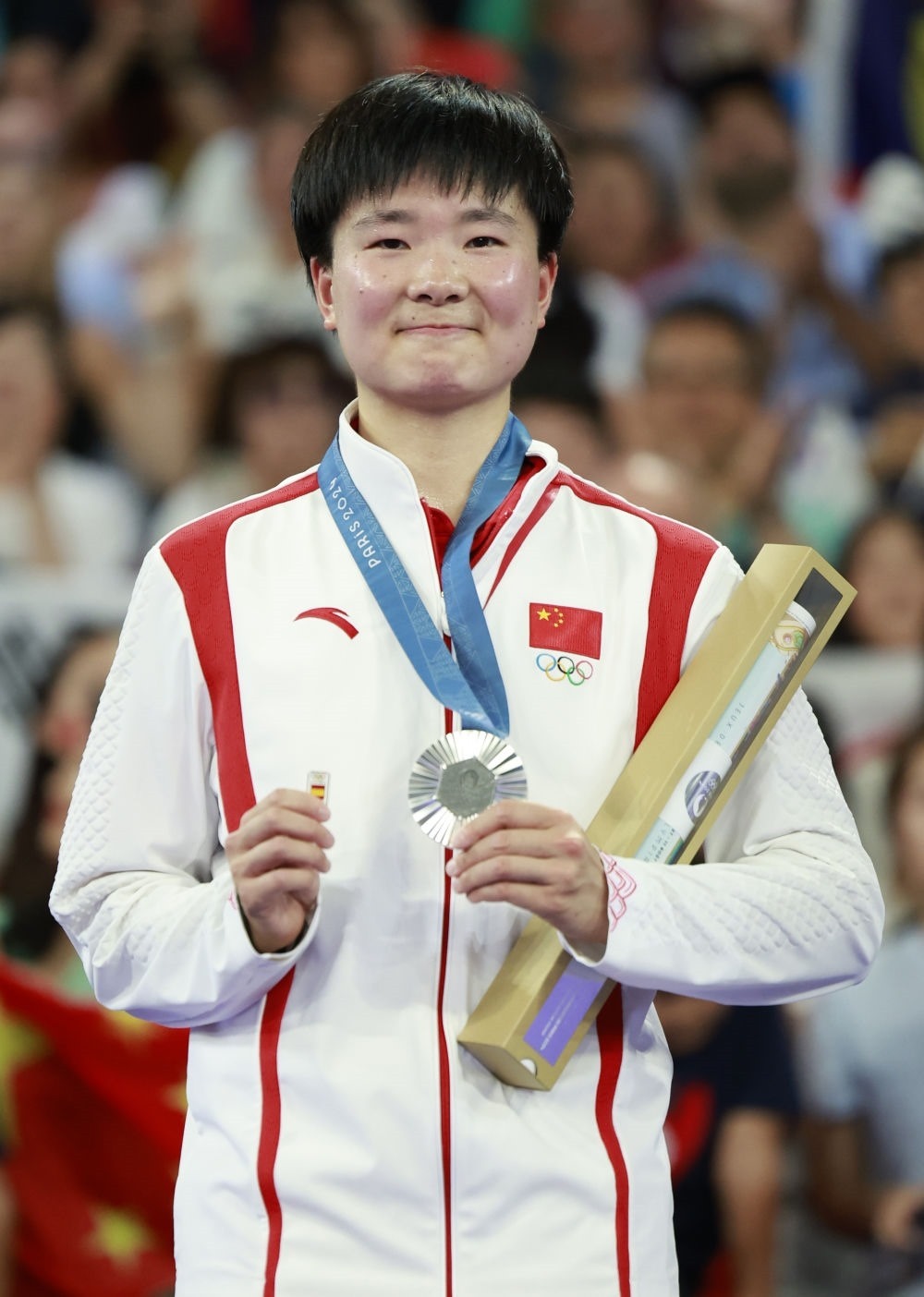 巴黎奧運(yùn)會(huì)羽毛球女子單打亞軍、中國選手何冰嬌在頒獎(jiǎng)儀式上一手握著銀牌，一手握著西班牙奧委會(huì)徽章（2024年8月5日攝）。新華社記者 任正來 攝