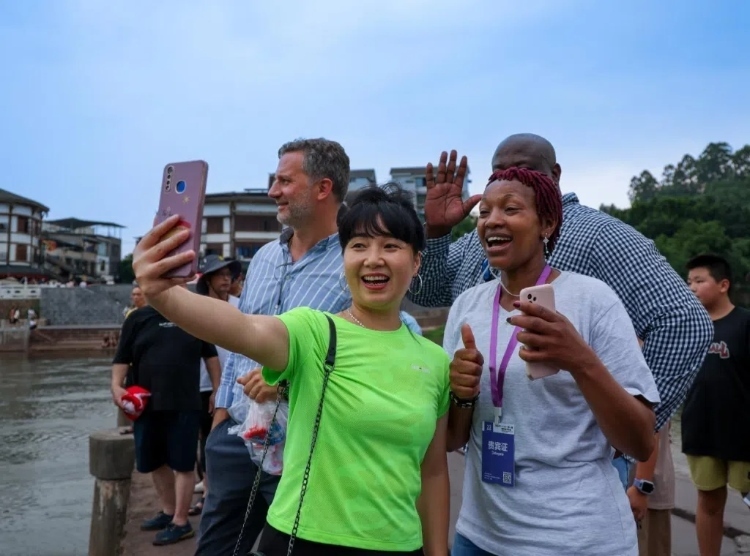 2024“一帶一路”媒體合作論壇聯(lián)合采訪調(diào)研行成員在樂山蘇稽古鎮(zhèn)與游客合影留念。本報(bào)記者 伊霄攝