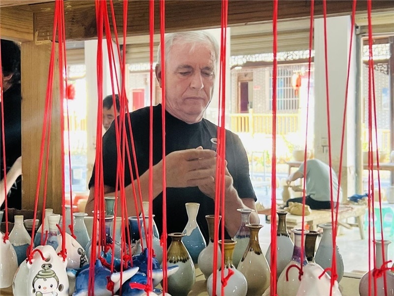 鄉(xiāng)愁如同一根根紅線，將游子與故鄉(xiāng)永遠(yuǎn)地牽連到一起?；逄账囄幕瘎?chuàng)意一條街的母氏陶藝館內(nèi)，紅線吊著陶瓶，思緒游走萬里。摩爾多瓦“信息標(biāo)簽”通訊社社長亞歷山大·塔納斯端詳著館內(nèi)展示的陶藝作品，并挑選出心儀的小擺件帶回摩爾多瓦，也帶走花茂村的“鄉(xiāng)愁”。（張亞欣攝）