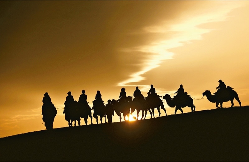 新時(shí)代以來(lái)，文化和旅游深度融合發(fā)展體制機(jī)制不斷健全，成功走出了一條獨(dú)具特色的中國(guó)旅游發(fā)展之路。圖為2024年9月1日清晨，游客在甘肅省敦煌市鳴沙山月牙泉景區(qū)乘騎駱駝，欣賞大漠風(fēng)光，體驗(yàn)絲路風(fēng)情。 新華社發(fā) 張曉亮/攝