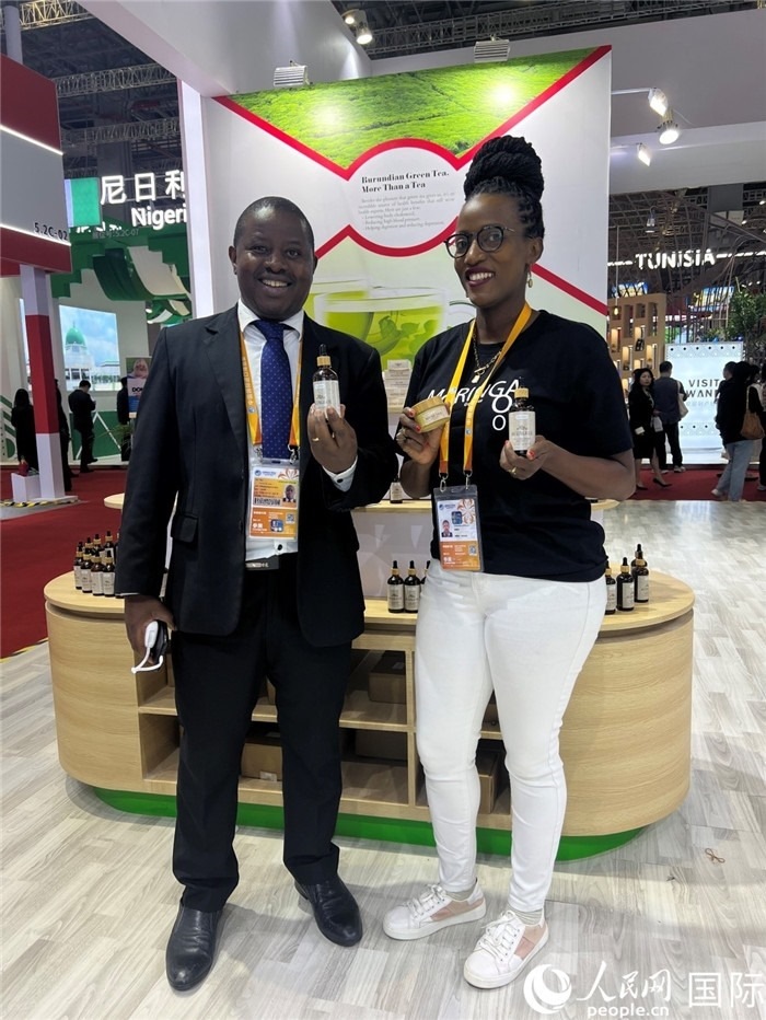 6月6日，布隆迪駐華大使館一等參贊布利馬索·阿爾弗雷德 (左，Bulimaso Alfred) 和參展商卡馬里扎·埃斯特拉 (Kamariza Estella) 在第七屆中國國際進(jìn)口博覽會布隆迪館展示當(dāng)?shù)厣a(chǎn)的辣木油。（人民網(wǎng) 艾里士 攝）